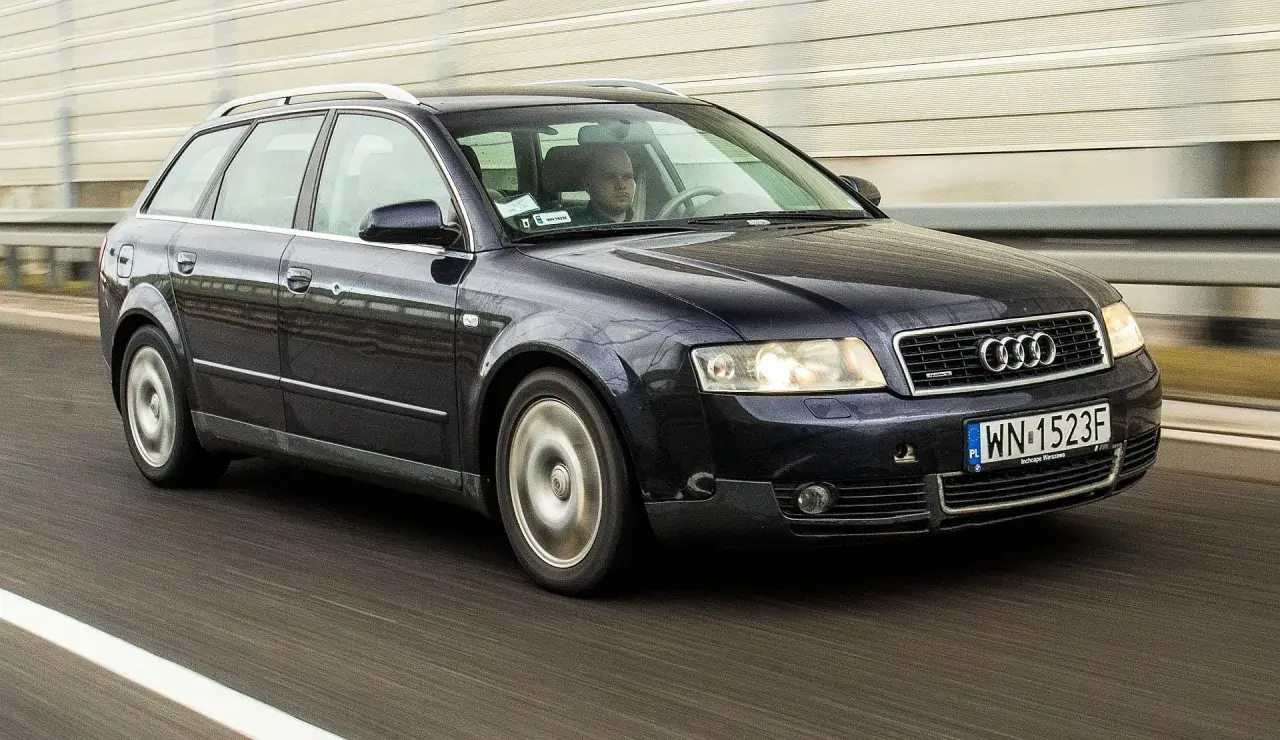 Ciemnogranatowe Audi B6 Avant pędzi autostradą. Kierowca skupiony na drodze.