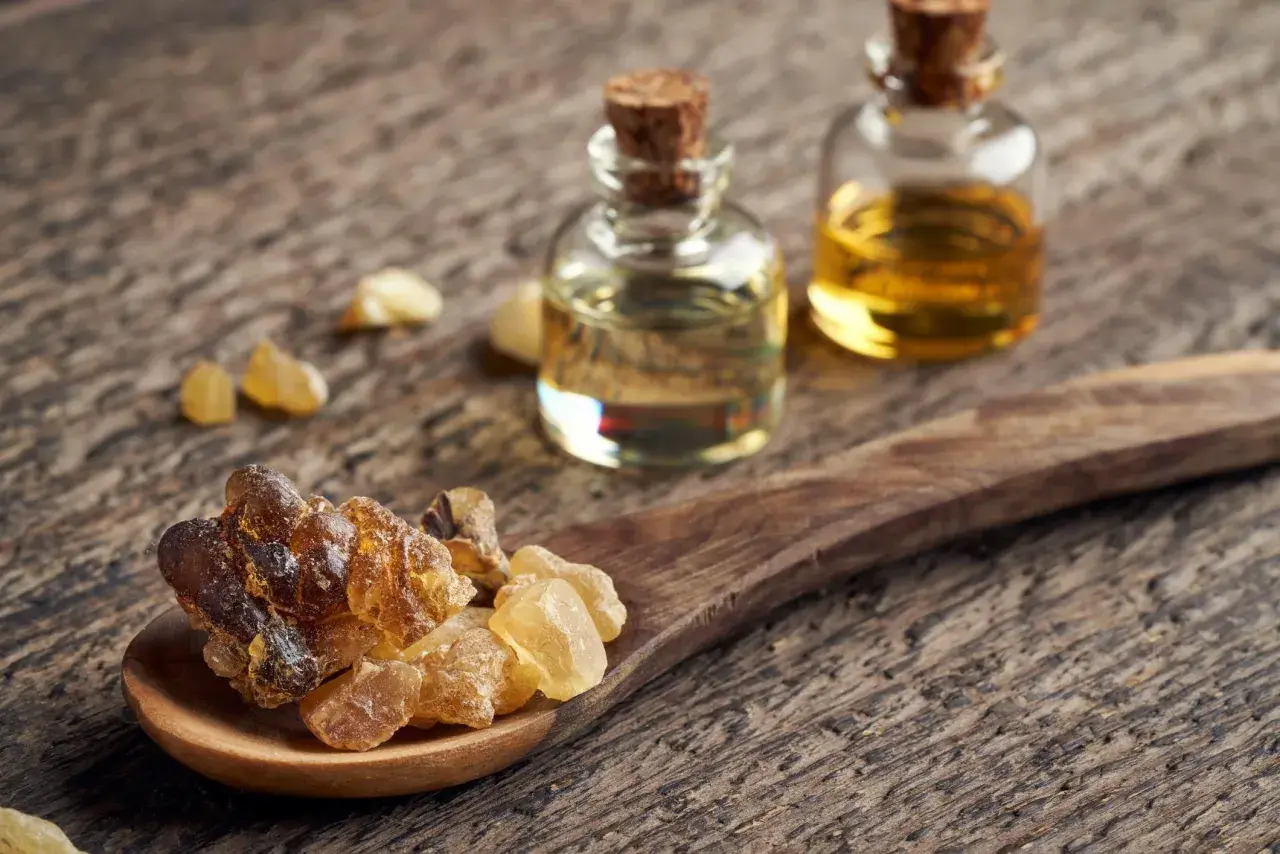 Resina di Boswellia Serrata su cucchiaio di legno, accanto a boccette di olio essenziale. Un integratore naturale.