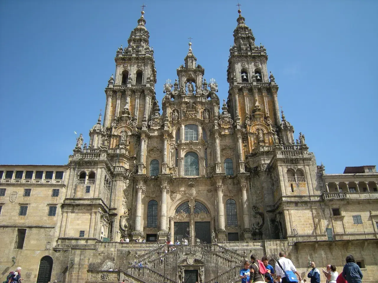 Majestatyczna katedra w Santiago de Compostela z trzema wieżami i schodami, po których wchodzą pielgrzymi.