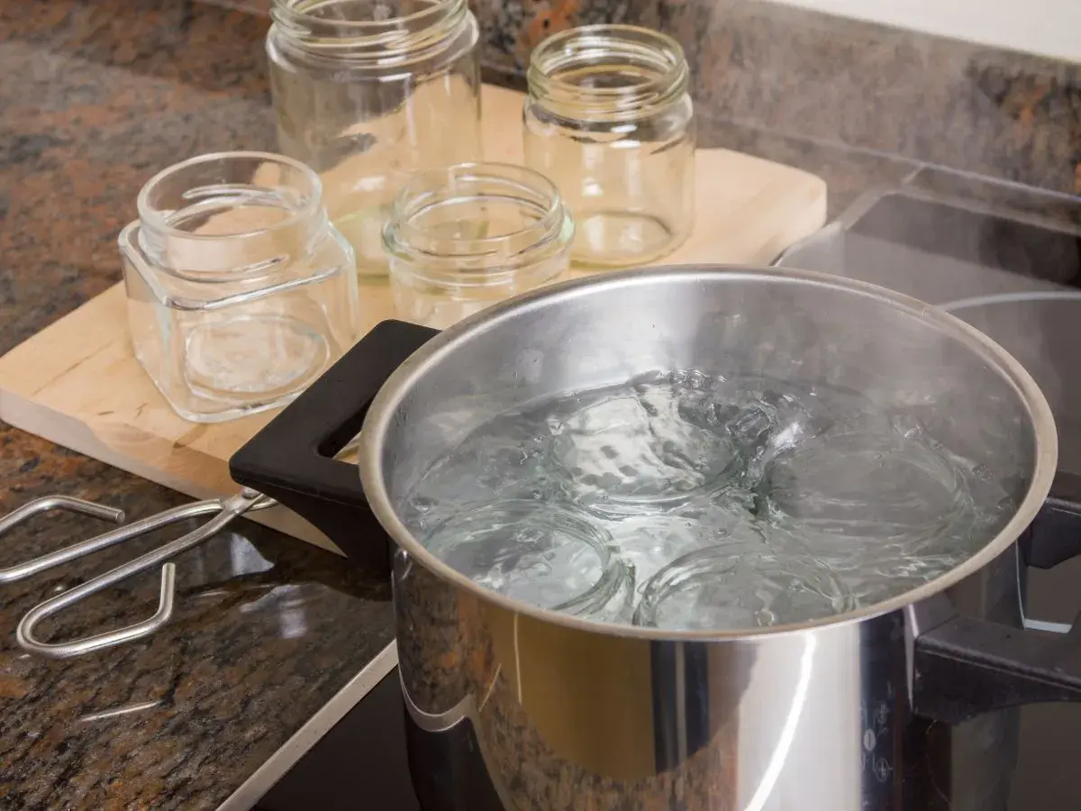 Gläser werden für das Einkochen mit Schraubdeckel sterilisiert. Ein Topf mit kochendem Wasser und ein Glasheber liegen bereit.