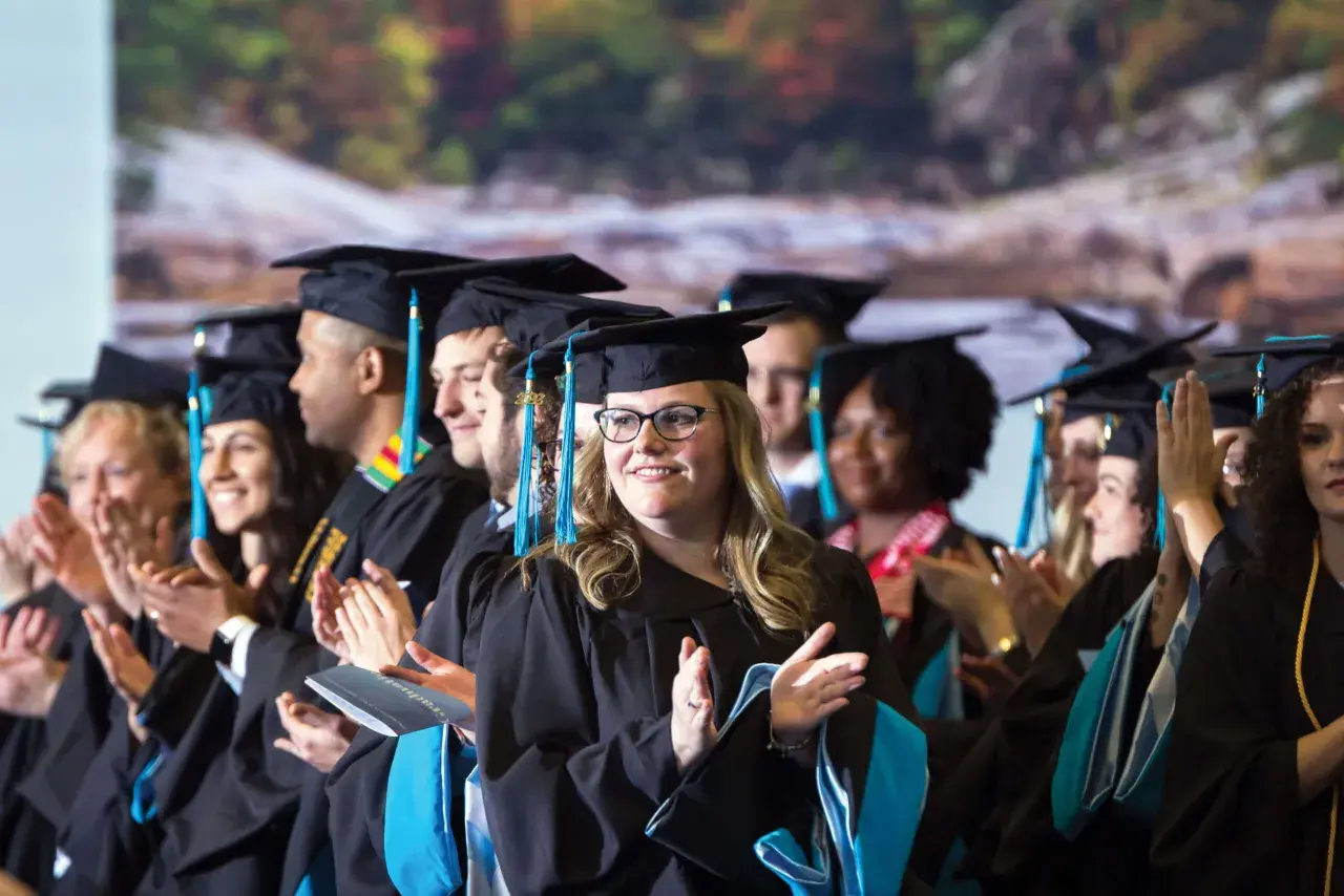 Graduates in caps and gowns applaud, celebrating their achievements in the UNC Chapel Hill online MPA program.