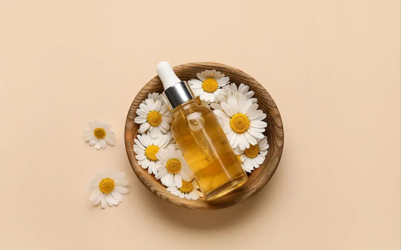 Flacon d'huile dorée entouré de marguerites dans un bol en bois. Le bisabolol, ingrédient clé, promet des bienfaits apaisants.
