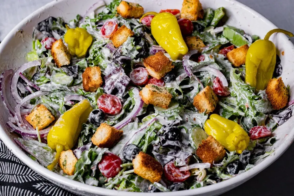 En krämig italiensk sallad till lasagne med gröna blad, tomater, rödlök, oliver, krutonger och gula peppar.