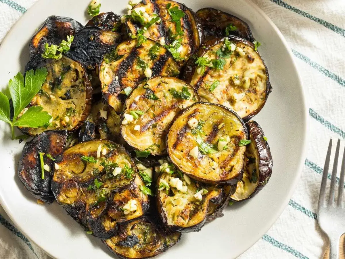 Rodajas de berenjenas a la plancha, doradas y tiernas, con ajo picado y perejil fresco. Un plato sencillo y delicioso.