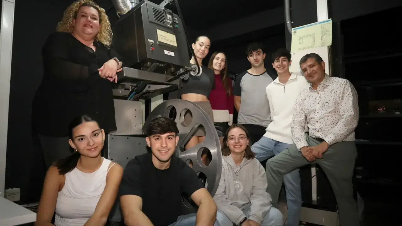Grupo de jóvenes y adultos posan junto a un proyector antiguo en el cine Cerbuna de Zaragoza.