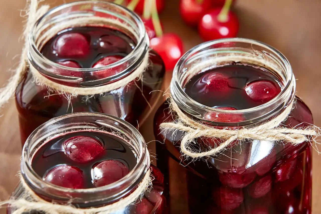Drei Gläser mit saftigen sauerkirschen einkochen, mit Juteband verziert, bereit für den Winter.