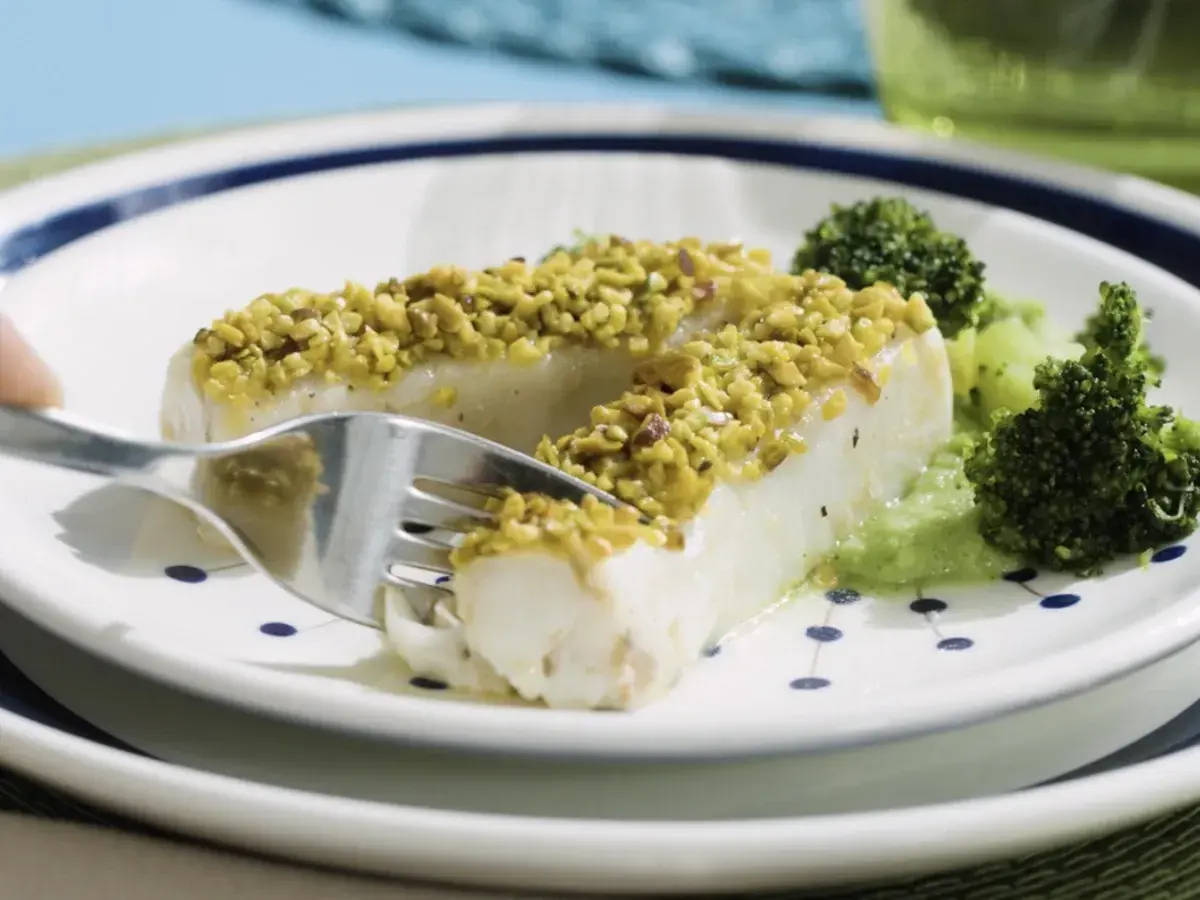 Filetti di merluzzo surgelati, impanati con pistacchi croccanti, serviti con broccoli e una salsa verde.