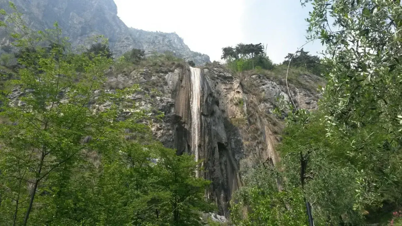 Cascata del Sopino, un velo d'acqua scende da una parete rocciosa circondata da vegetazione lussureggiante.