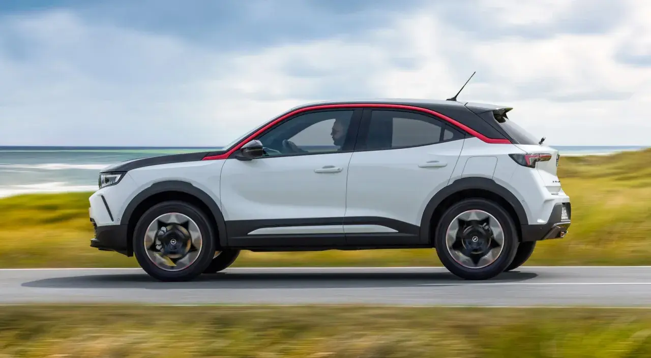 Opel Mokka blanco con detalles rojos, conduciendo por la costa. Las opiniones sobre este coche son muy positivas.