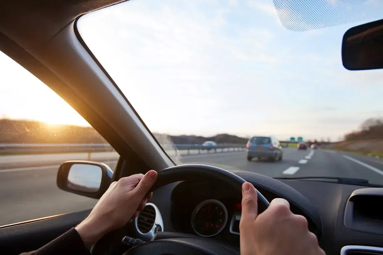 Ręce na kierownicy Toyoty Corolli, słońce zachodzi na autostradzie. Jak włączyć tempomat?