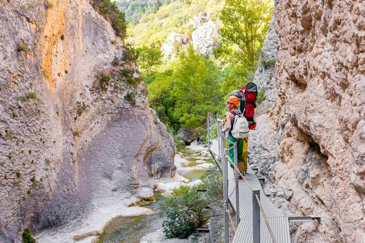 Senderistas disfrutan de las **pasarelas del Vero**, un camino metálico que serpentea por un cañón rocoso con un río cristalino.