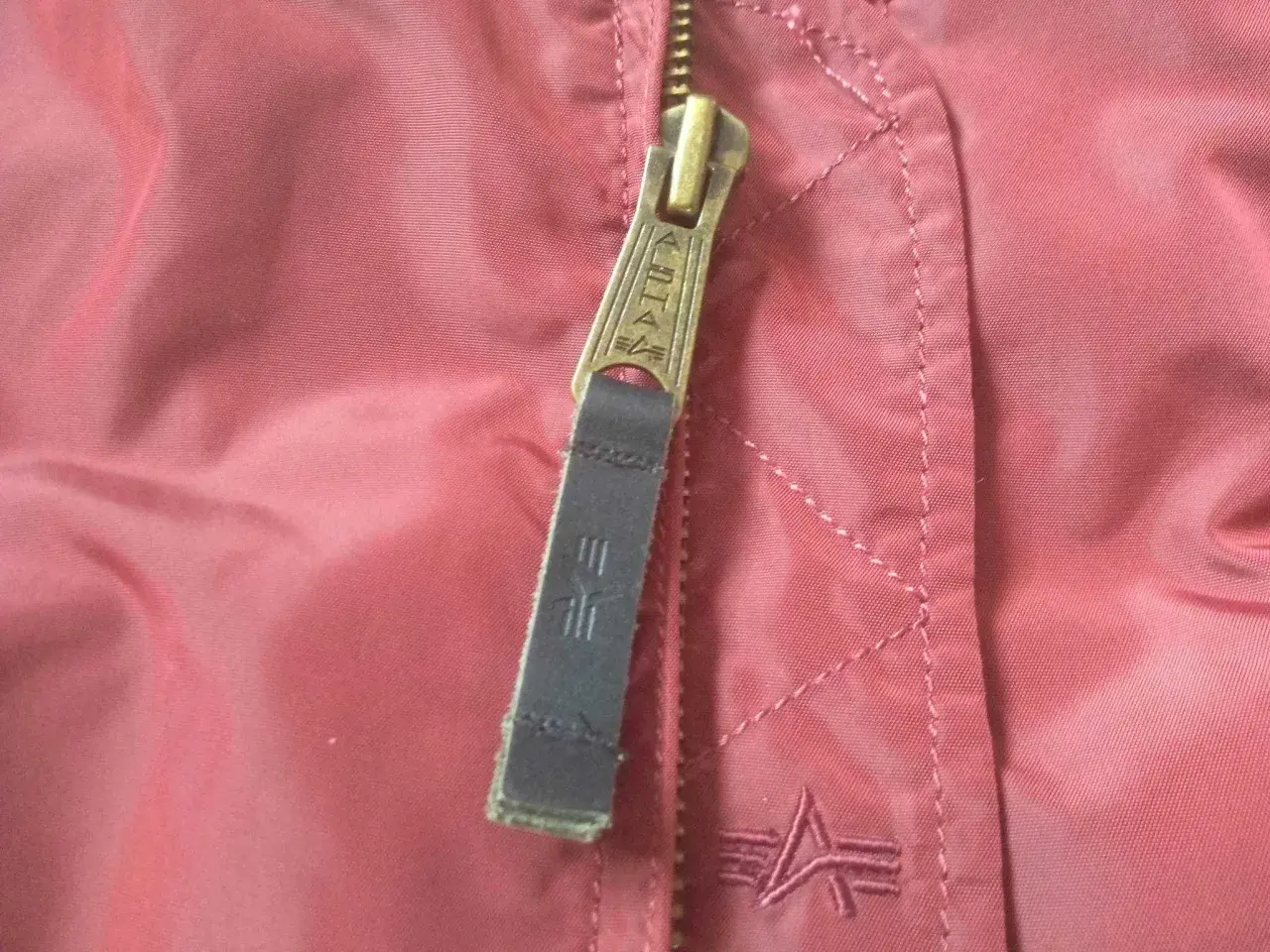 Zamek kurtki Alpha Industries z logo. Detale materiału i szwów, pomocne przy wyborze alpha industries rozmiarówka.