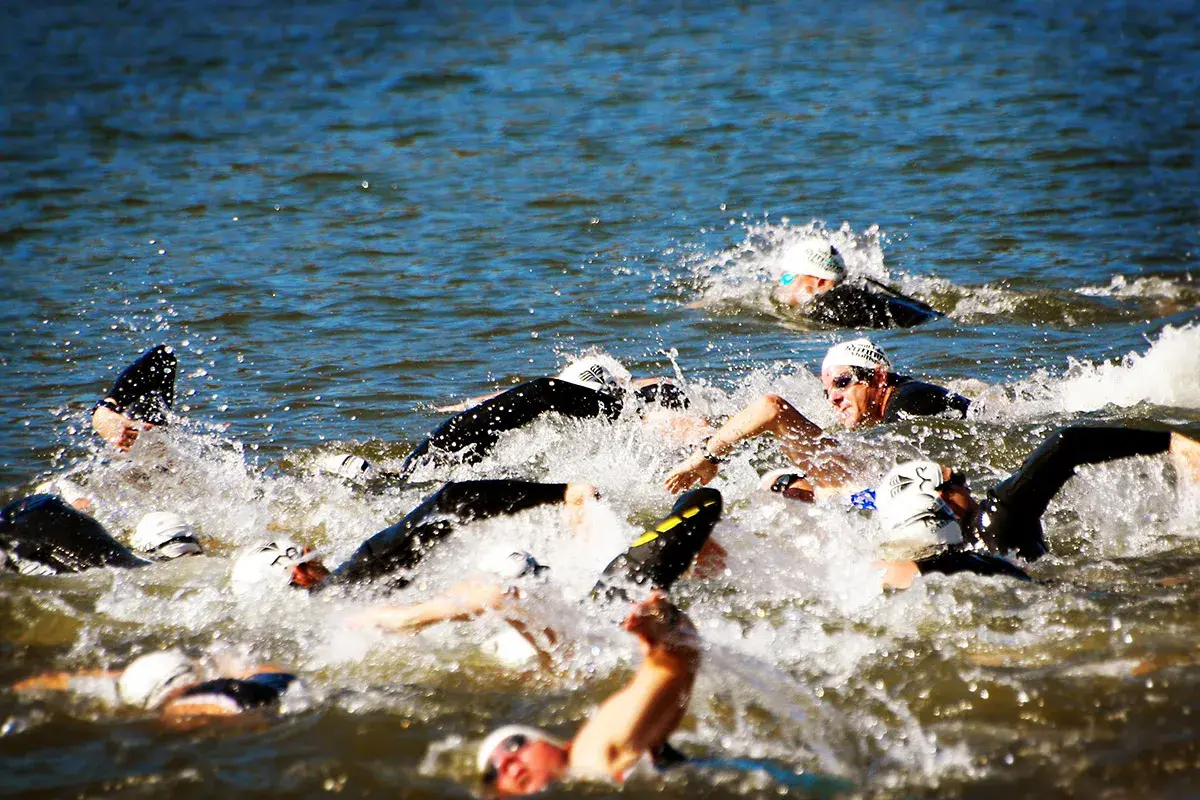 Zawodnicy walczą o pozycję podczas pływania na dystansie 1/2 ironman. Woda wzburzona, widać kaski i okulary.