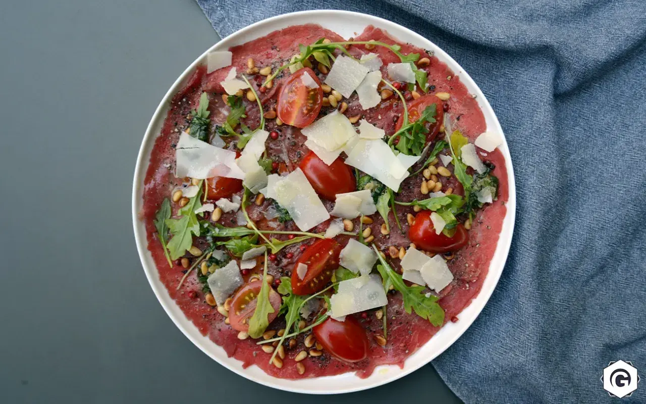 Carpaccio de bœuf finement tranché, garni de tomates cerises, roquette, pignons de pin et copeaux de parmesan. Un délice visuel et gustatif.