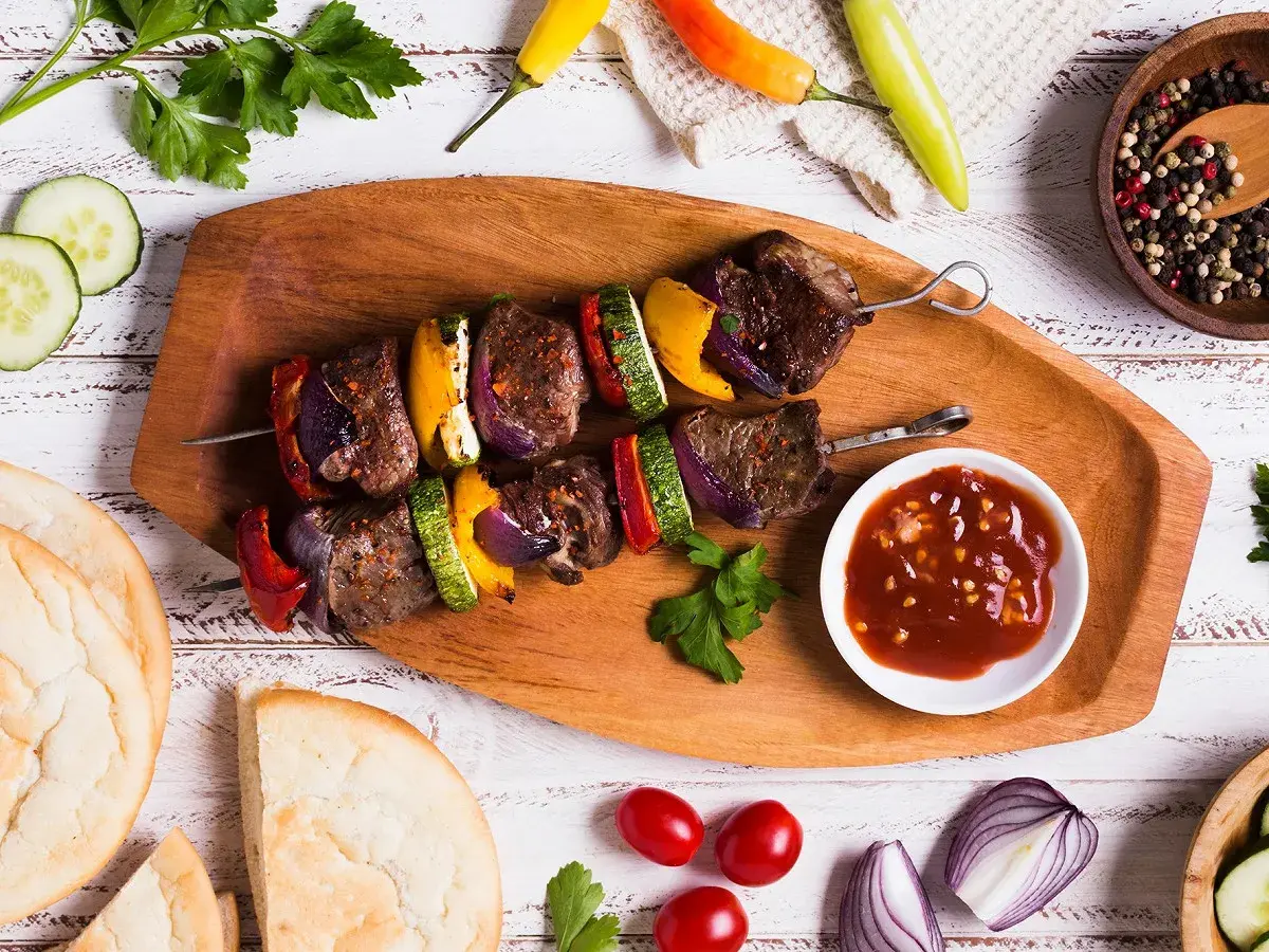 Brochette de rumsteck grillée avec poivrons, courgettes et oignons, servie avec une sauce savoureuse.