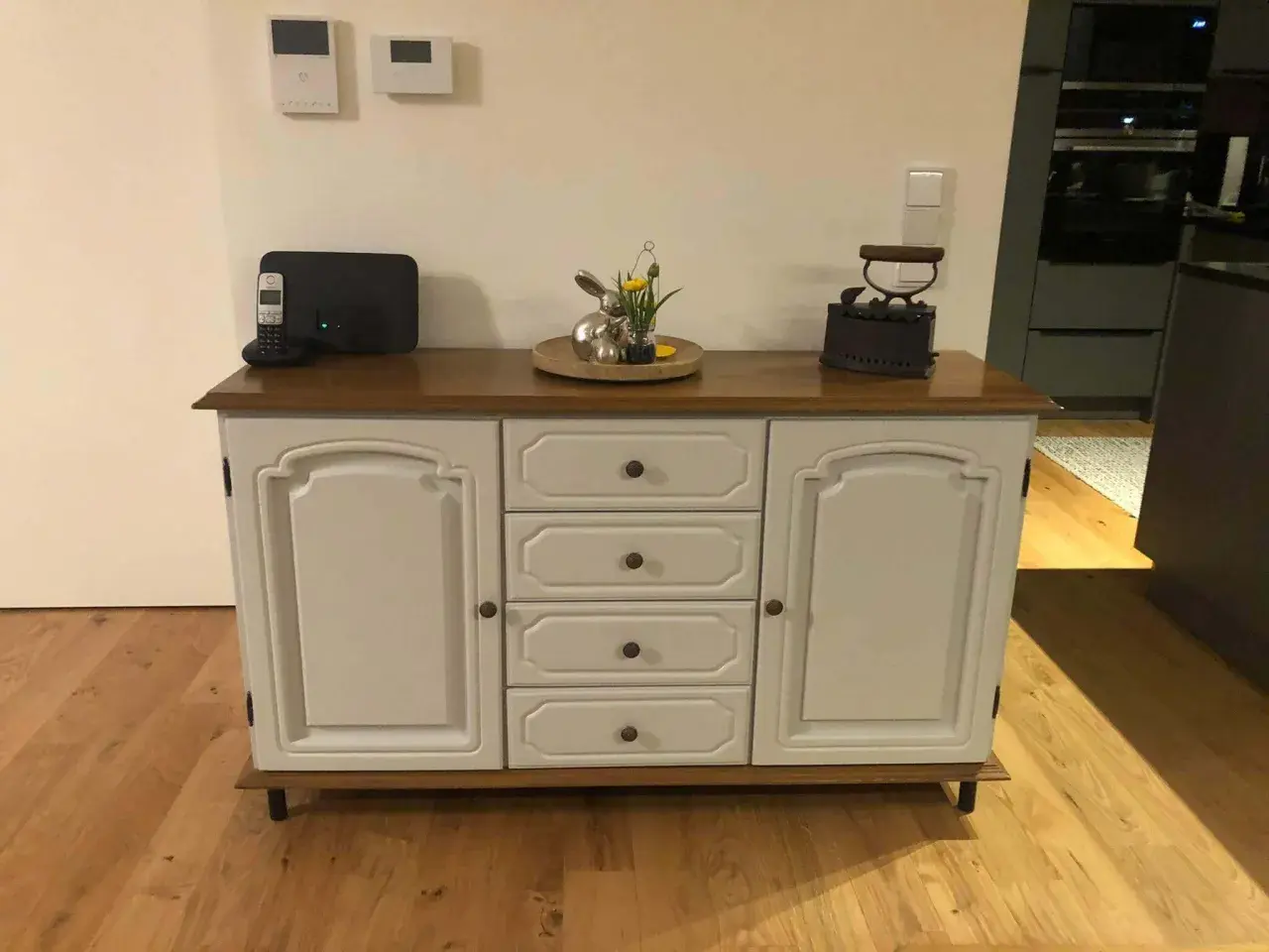 Ein Sideboard mit Eichenholzplatte, das rustikal und modern kombiniert. Darauf ein Osterhase, ein Bügeleisen und ein Telefon.