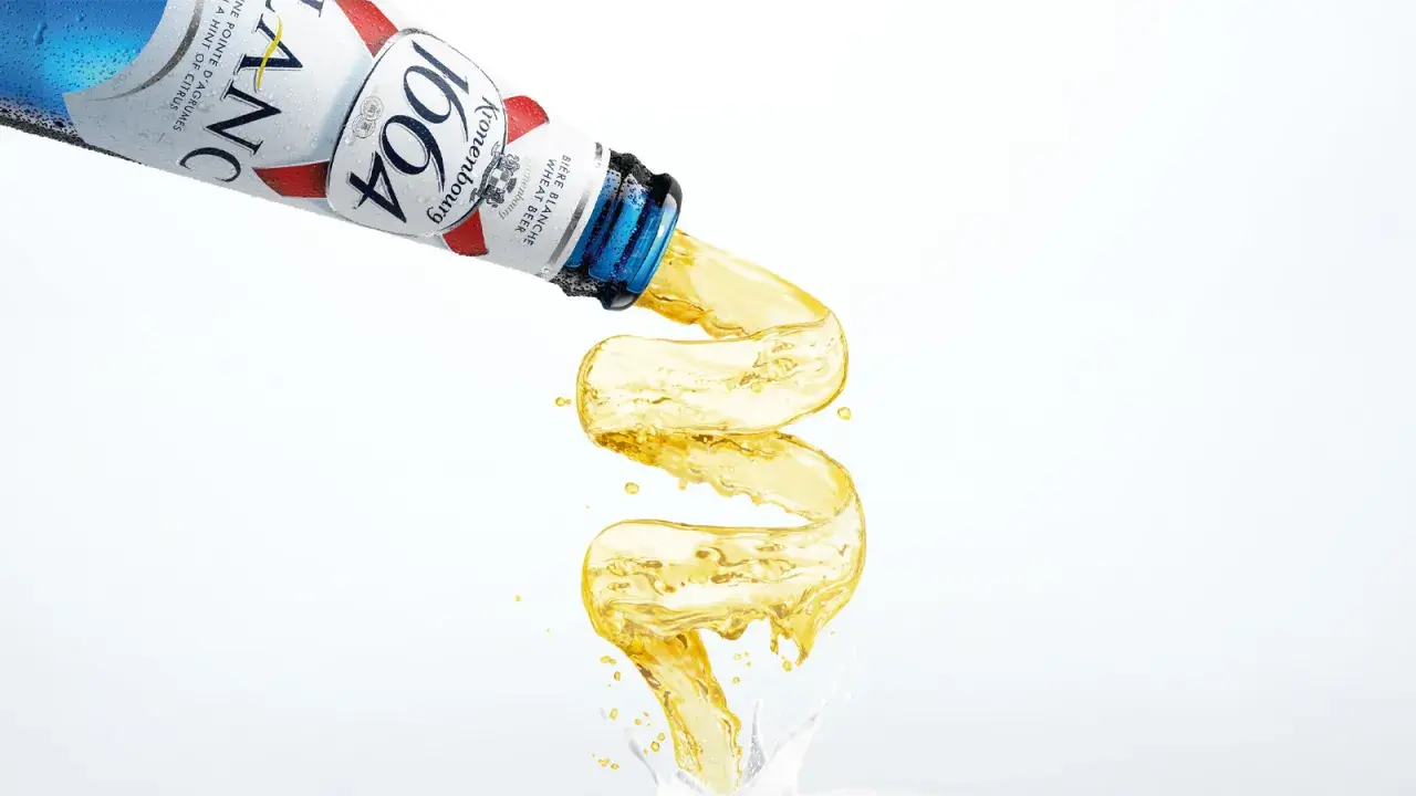 Piwo w niebieskiej butelce Kronenbourg 1664 leje się w fantazyjny sposób, tworząc złoty strumień.
