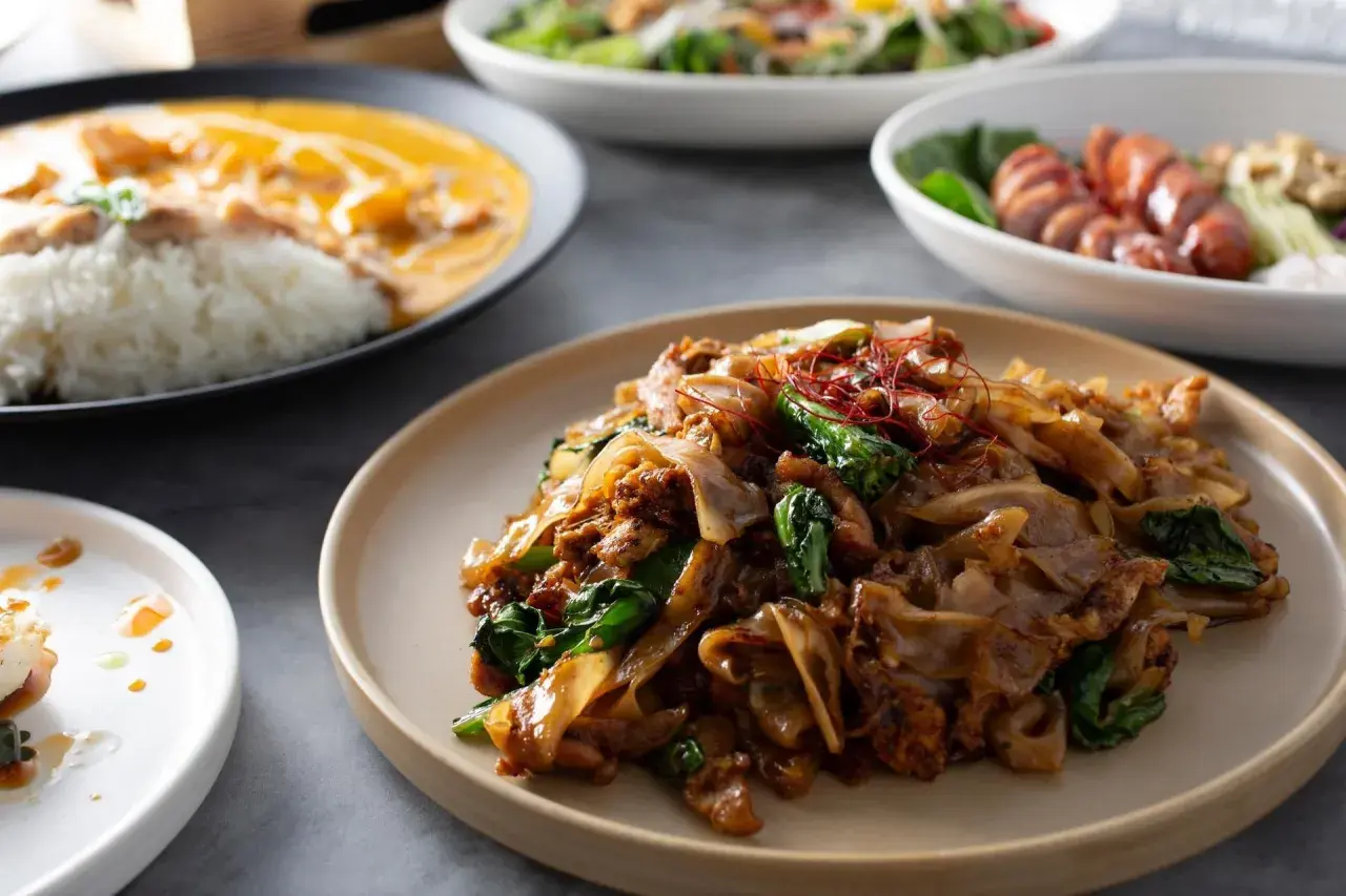 Talerz z aromatycznym makaronem tajskim, polanym sosem, z dodatkiem zielonych warzyw i czerwonych nitek chili.