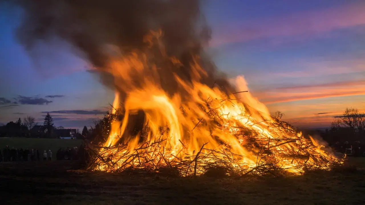 Ein riesiges Osterfeuer lodert im Abendrot. Menschen versammeln sich, um diese alte Osterfeuer Tradition zu erleben.