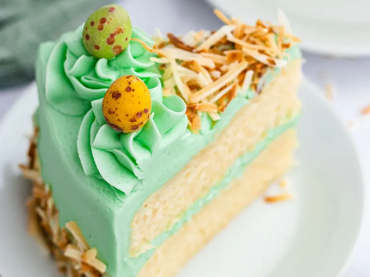 Rebanada de pastel verde menta con glaseado, decorada con huevos de pascua y coco tostado. ¡Ideas de pasteles de Pascua!