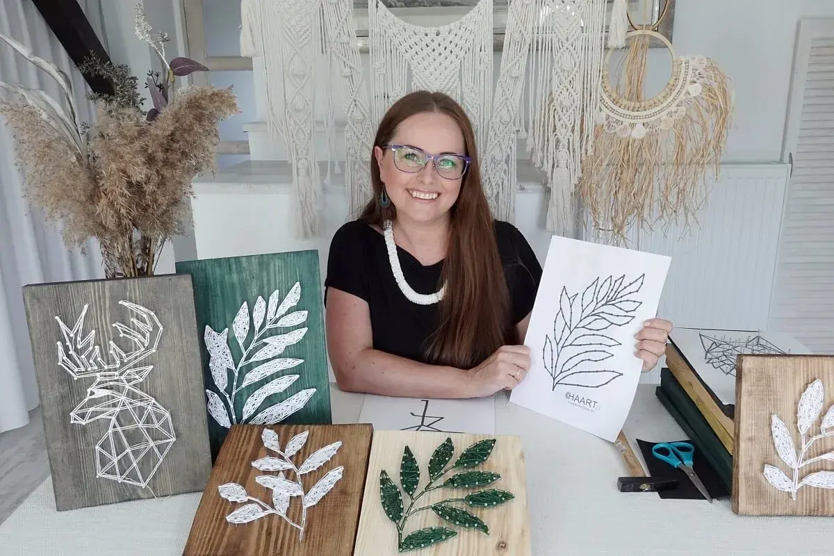 Kobieta prezentuje swoje prace string art, w tym jelenia i liście. Pokazuje też szablony do string art, które pomagają tworzyć piękne dekoracje.