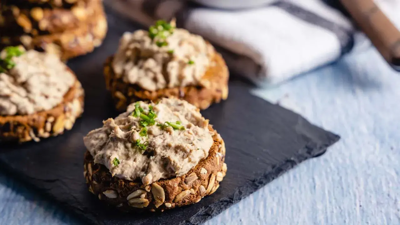 Deliciosos canapés con atún vegano cremoso y cebollino fresco sobre pan integral con semillas.