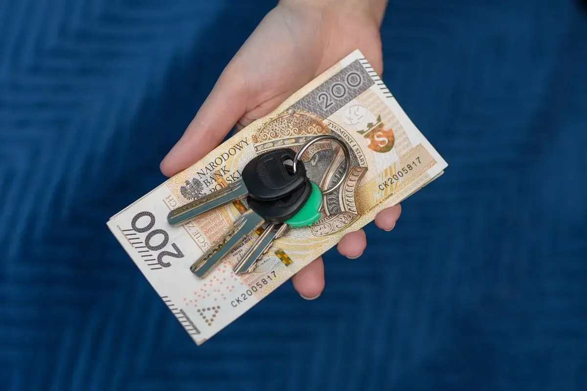 Dłoń trzyma banknot 200 zł i klucze. Symbolizuje to zsl rejestracja, np. kupno samochodu.