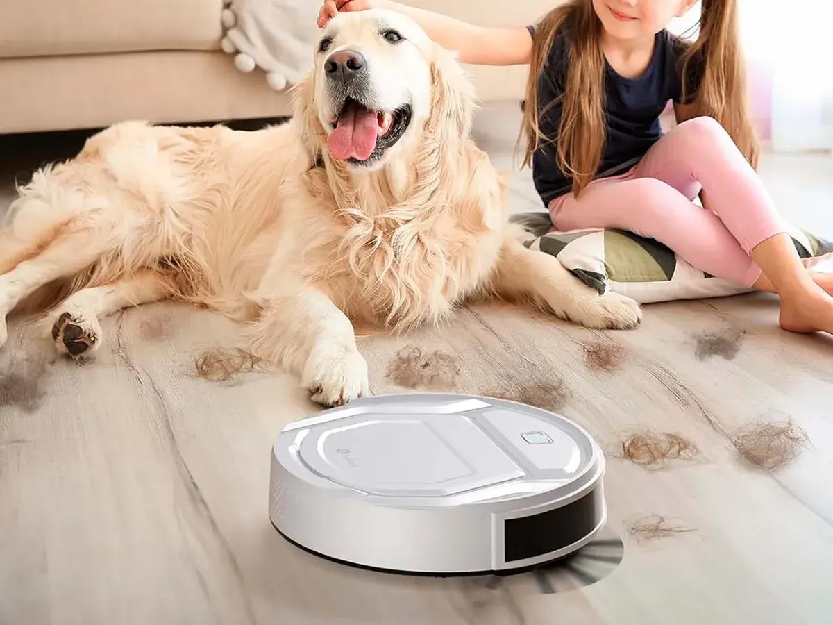 Un robot aspirador limpia el pelo de perro en un hogar mientras una niña acaricia a su mascota.