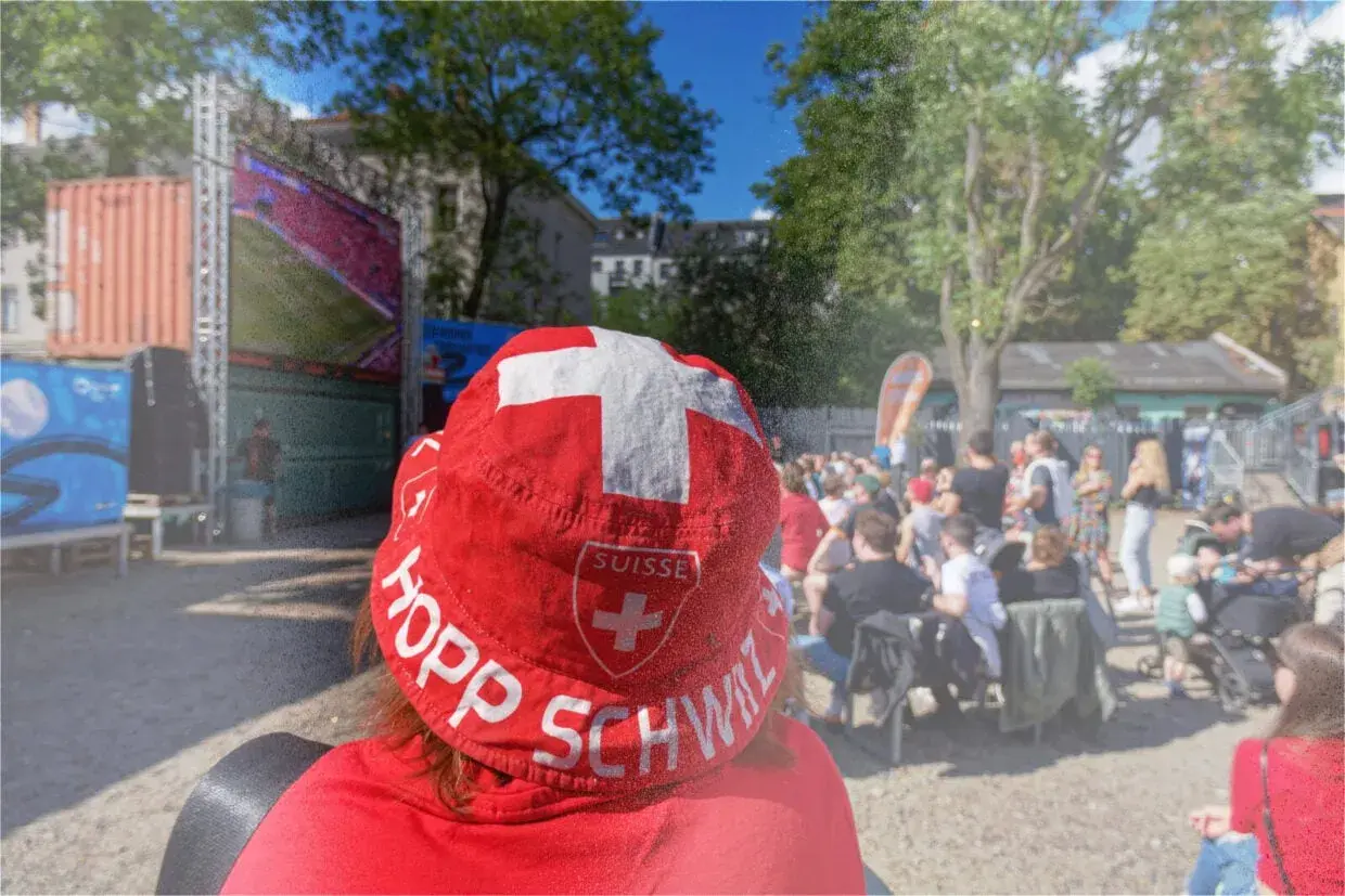 Public viewing Berlin: Ein Fan mit Schweizer Hut jubelt bei einem Fußballspiel.