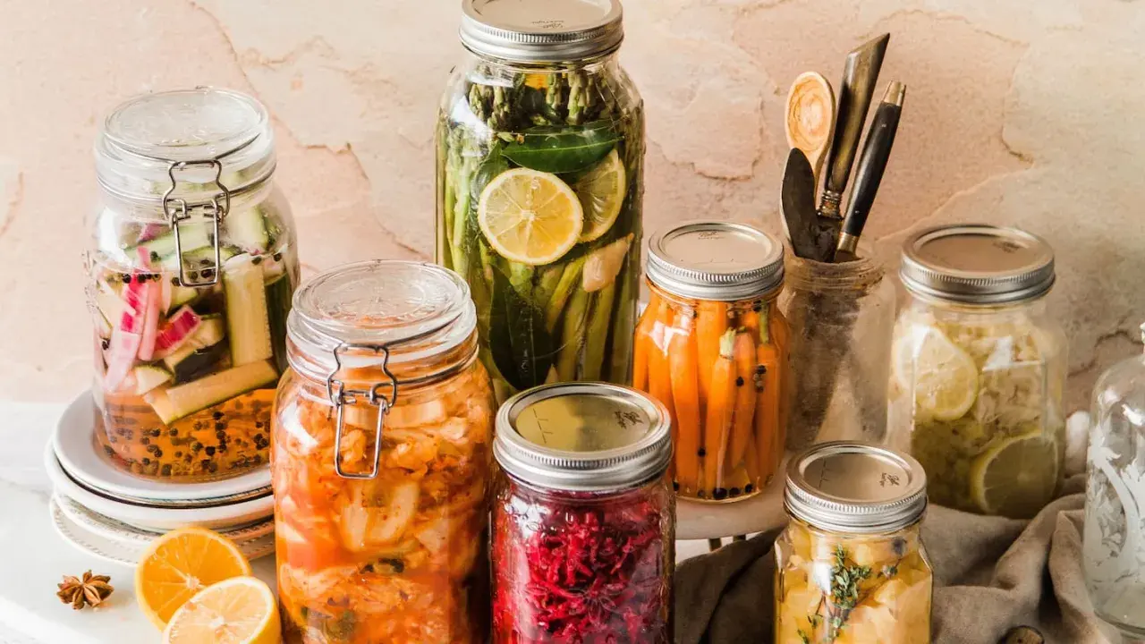 Eingemachtes Gemüse in Gläsern: Karotten, Gurken, Spargel, Kimchi und mehr. Was kann man nicht einkochen? Frische Kräuter und Zitronenscheiben geben Aroma.