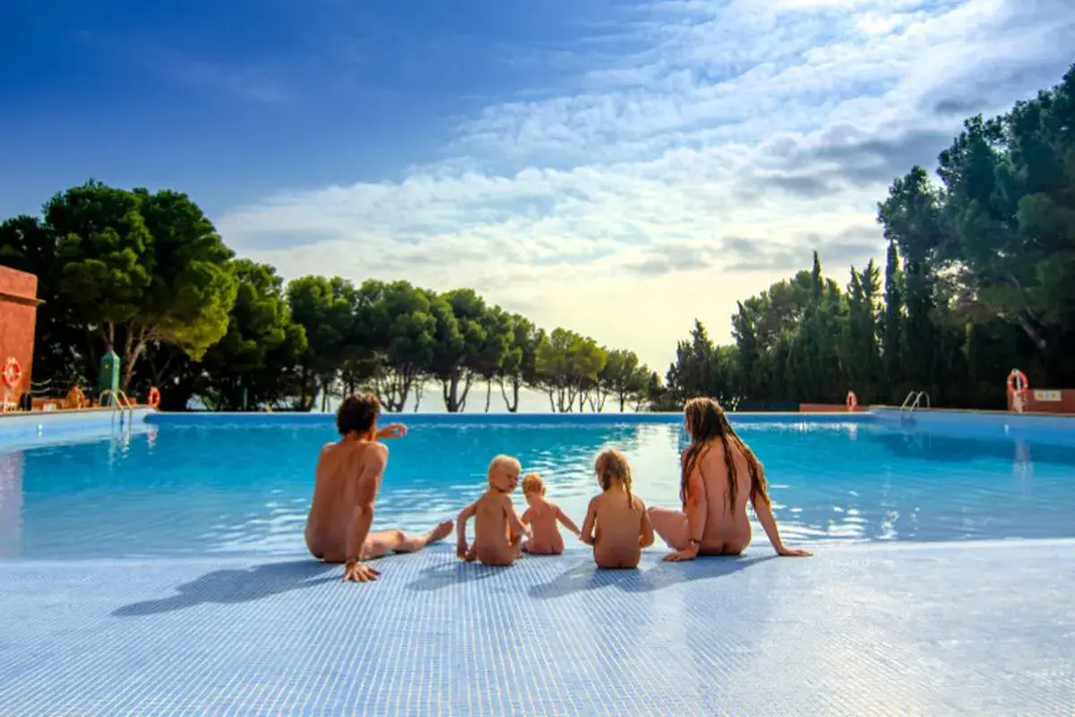 Famille profitant d'une journée ensoleillée au bord de la piscine dans un camping naturiste au Portugal.