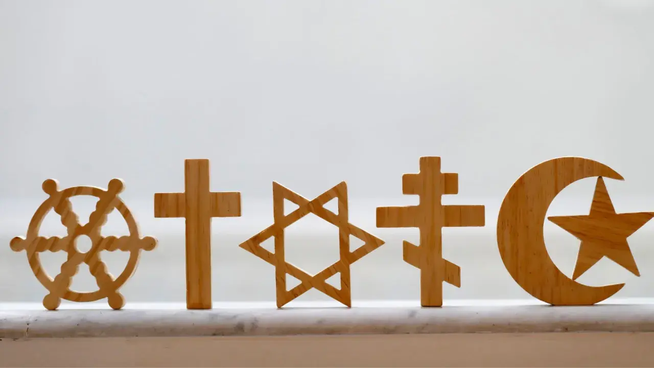 Drewniane symbole religijne: koło Dharmy, krzyże, Gwiazda Dawida, półksiężyc z gwiazdą. Pokazują różnorodność wierzeń, jak w Bangladeszu religia.
