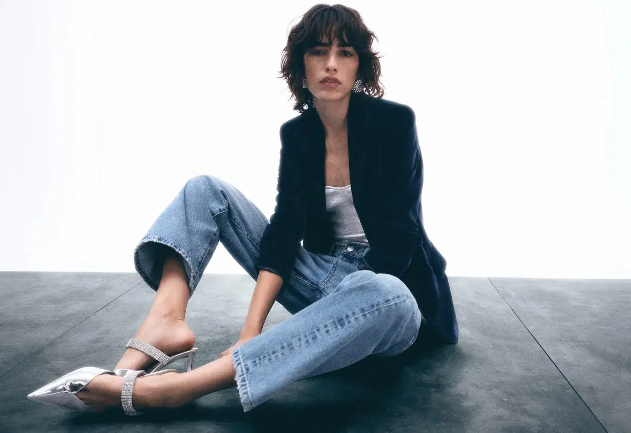 Frau in lässigen Jeans, Samtblazer und glitzernden Mules. Ein Look, der casual chic perfekt verkörpert.