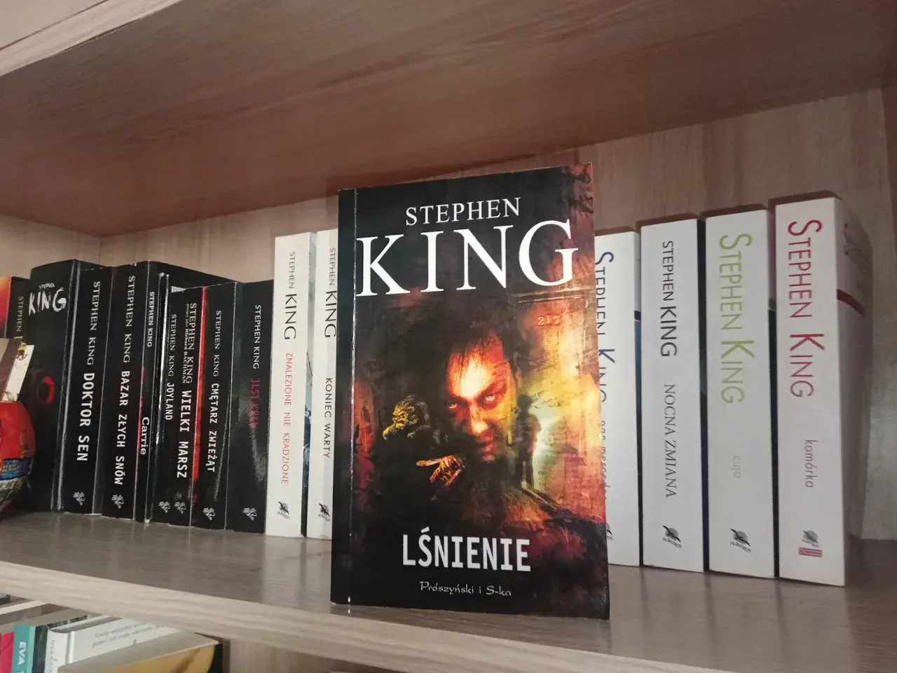 Książki Stephena Kinga na półce, w tym "Lśnienie" z przerażającą okładką.