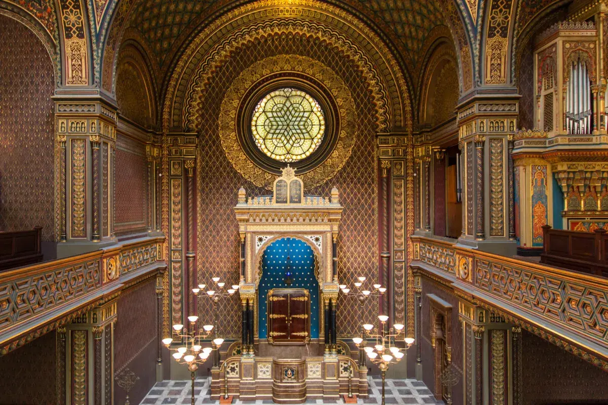 Intérieur orné de la synagogue espagnole de Prague, avec un vitrail circulaire, un Aron Kodesh bleu et des lustres dorés.