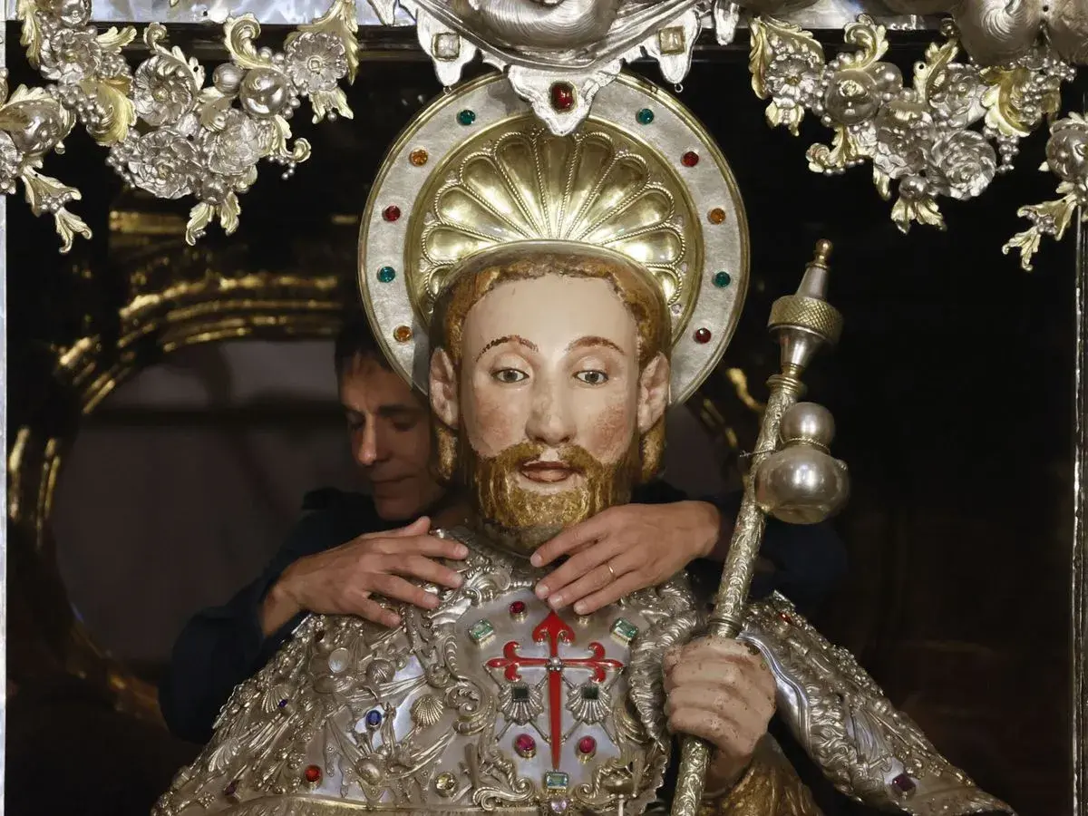 Un hombre ajusta una figura religiosa adornada, quizás preparándola para una celebración que se celebra hoy en España.