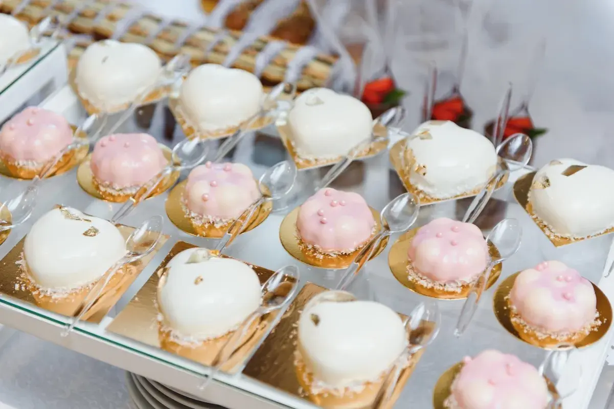 Eleganckie finger food w kieliszkach: serduszka i kwiatki w białej i różowej polewie, ozdobione perełkami i płatkami złota.