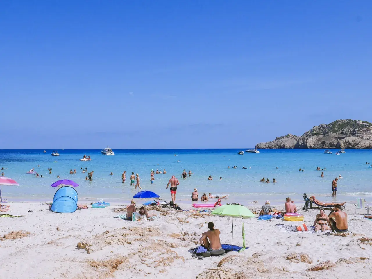 Słoneczna plaża na Majorce, pełna ludzi kąpiących się i opalających. Idealne miejsce na wakacje z dziećmi, oferujące mnóstwo atrakcji.