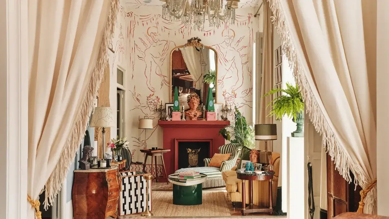 Salon éclectique avec papier peint aux figures rouges, cheminée rouge, mobilier ancien et moderne, rideaux à franges.
