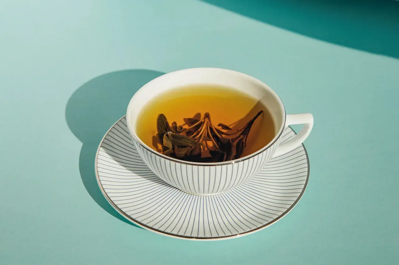 Eine Tasse Kräutertee mit Salbeiblättern, die ihre wohltuende tee wirkung entfalten. Das Geschirr ist weiß mit blauen Streifen.