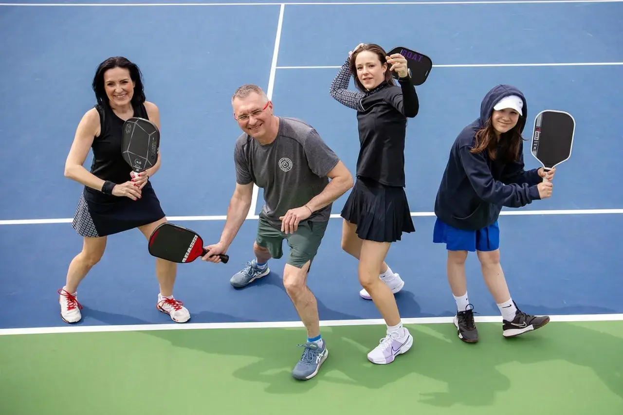 Rodzina na korcie do pickleball, co to za sport? Wszyscy trzymają rakietki, gotowi do gry.