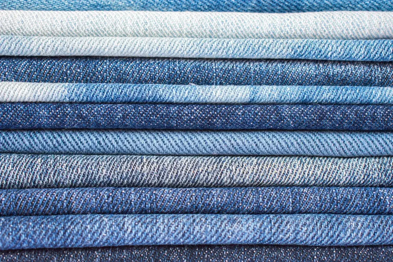 Pile de jeans bleus de différentes teintes. Le jean est fait de coton, un tissu résistant et confortable.