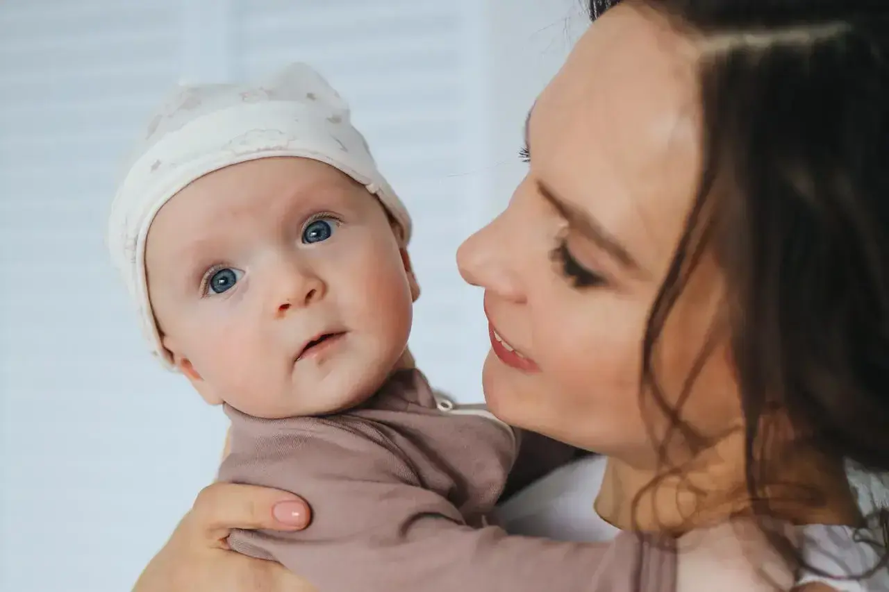 Mama z czułością tuli dziecko. Poradnik: jak nauczyć dziecko ssać pierś po butelce, by karmienie było łatwe i przyjemne.