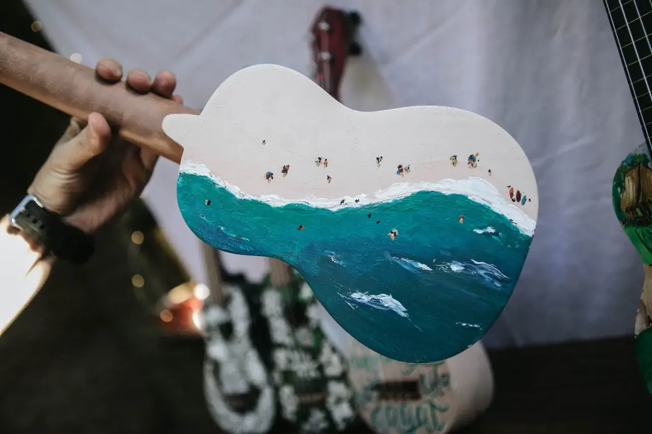 Un ukulélé peint d'une scène de plage animée. La taille ukulele est parfaite pour emporter cette œuvre d'art en voyage.
