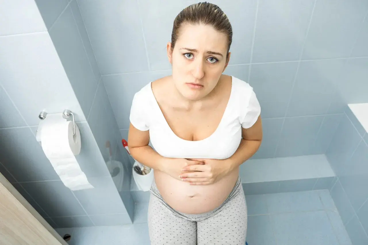Femme enceinte au premier trimestre, le visage marqué par l'inconfort, se tenant le ventre. La constipation grossesse 1er trimestre est une réalité pour beaucoup.