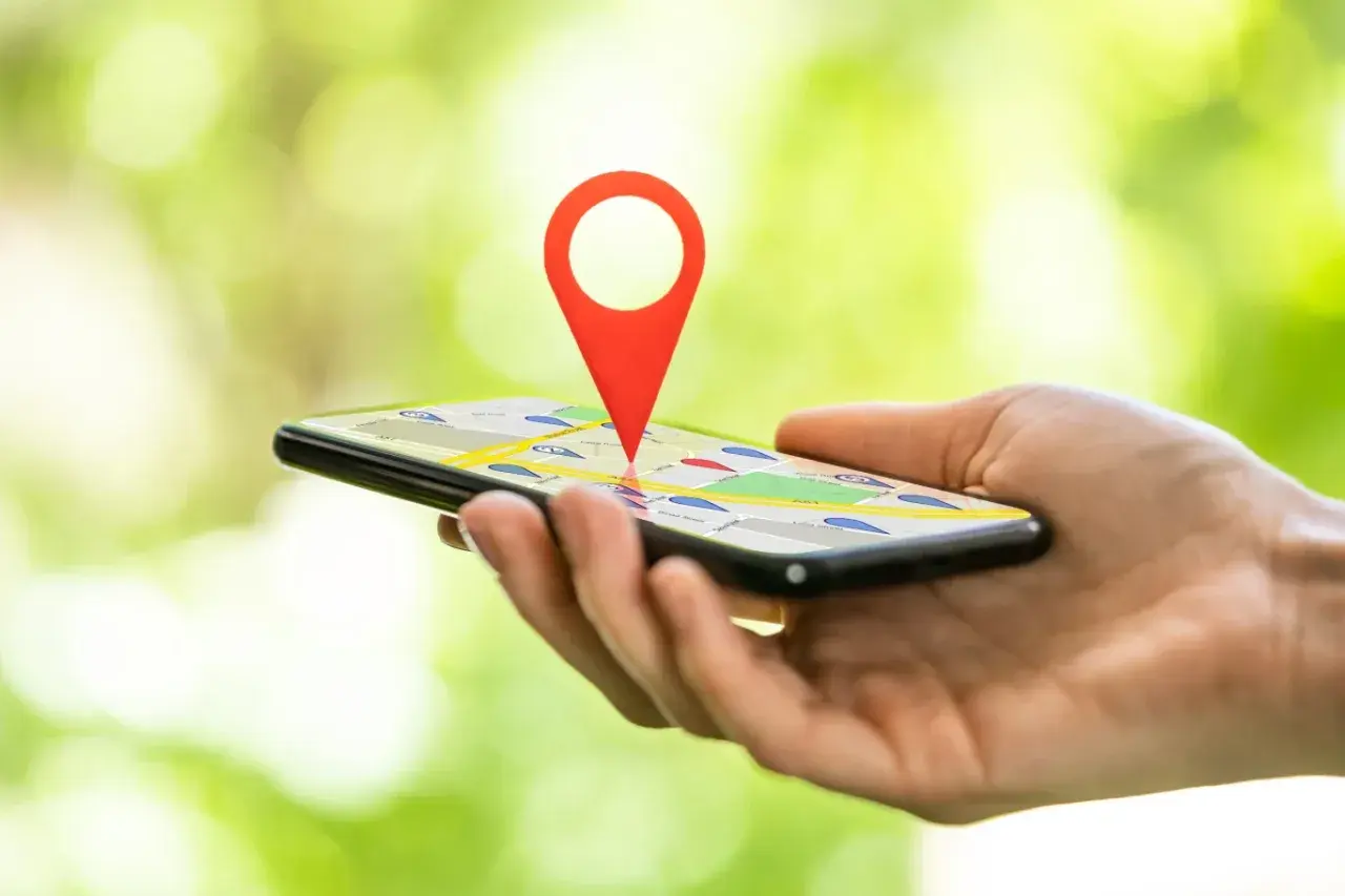 Dłoń trzyma smartfon z mapą i czerwoną pinezką. Dowiedz się, jak zlokalizować telefon przez Google.