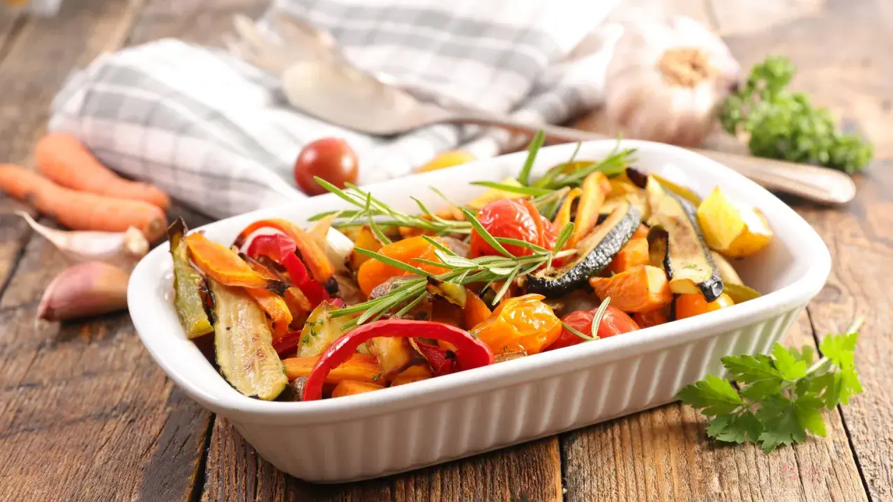 Un plato blanco lleno de coloridas verduras al horno, con romero fresco y tomates cherry.