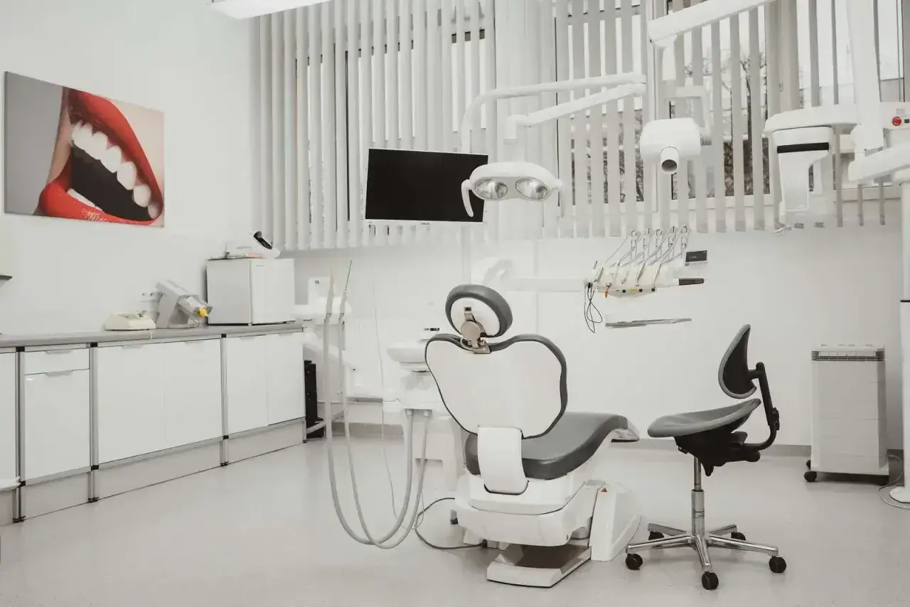 Nowoczesny gabinet stomatologiczny i ortodontyczny. Biały fotel dentystyczny, lampa, unit i szafki. Obraz z uśmiechem na ścianie.