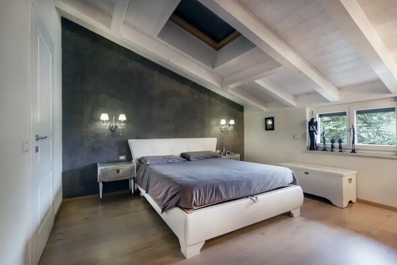 Camera da letto accogliente in un sottotetto non abitabile, con travi a vista, lucernario e pareti in resina.
