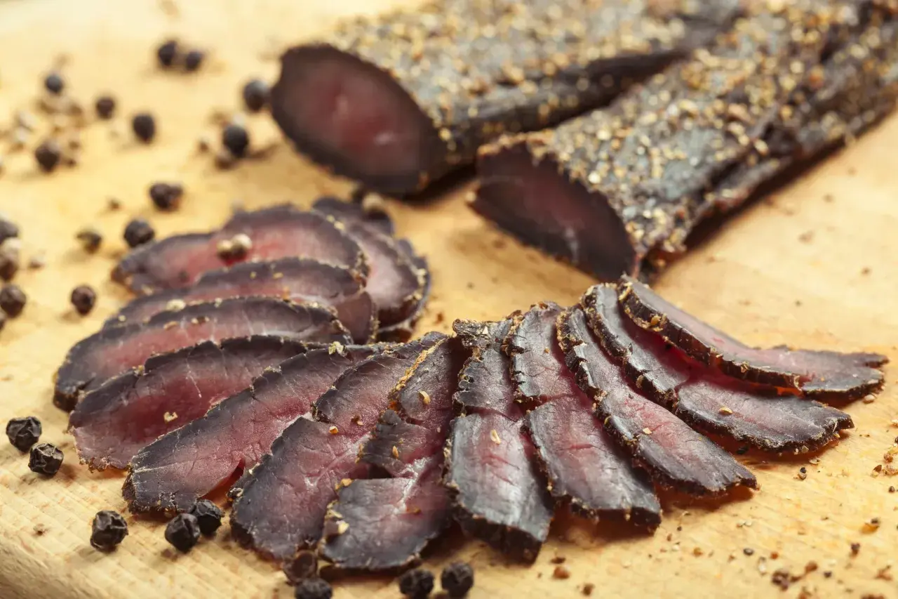 Tranches de filet mignon séché, assaisonnées de poivre noir, disposées sur une planche en bois.